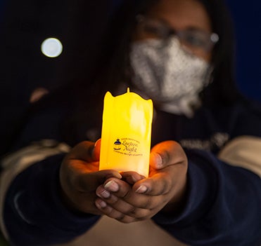 A Black woman in face covering holds out LED lantern to camera