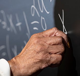Hand writes an "x" with white chalk on blackboard