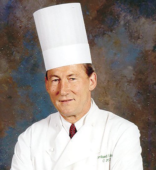 man wearing white coat, tie and chef's hat
