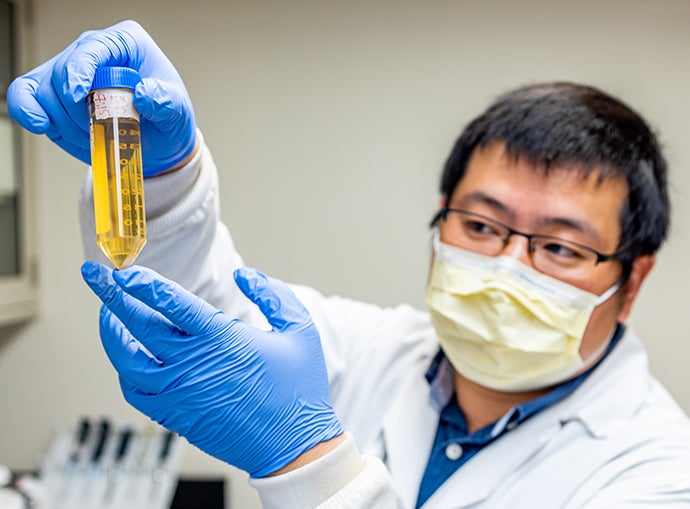 Masked scientist in blue gloves holds amber-colored measuring tube