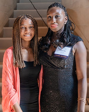 Omolara wearing a salmon cardigan and black dress and Aisha wearing a black lace dress, standing in front of steps inside Heinz Memorial Chapel